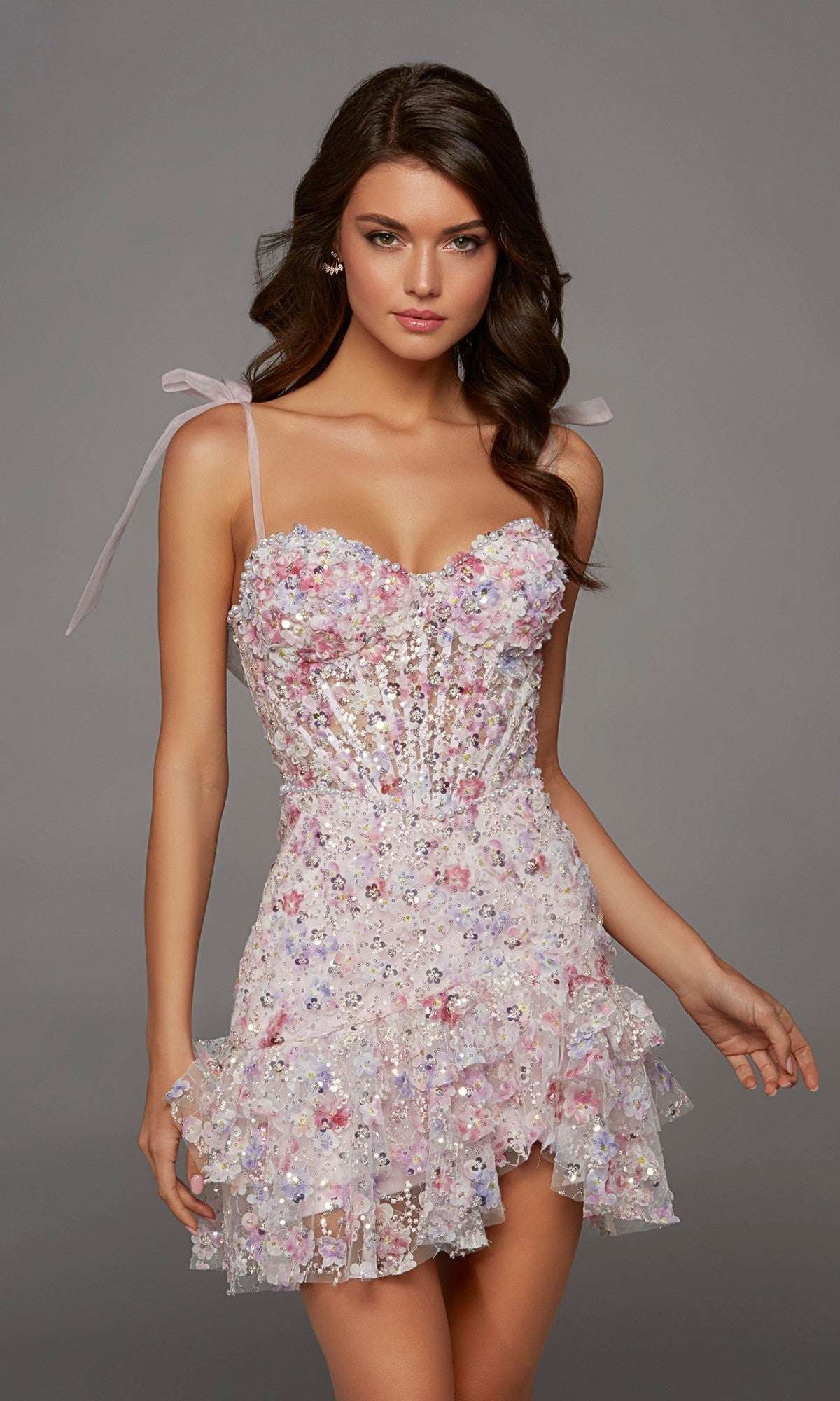 A woman poses against a plain gray background wearing the Alyce 30111 Short Homecoming Dress in pink—a sleeveless mini dress adorned with floral embellishments and featuring a ruffled hem, evoking the elegance of a cocktail party ensemble.